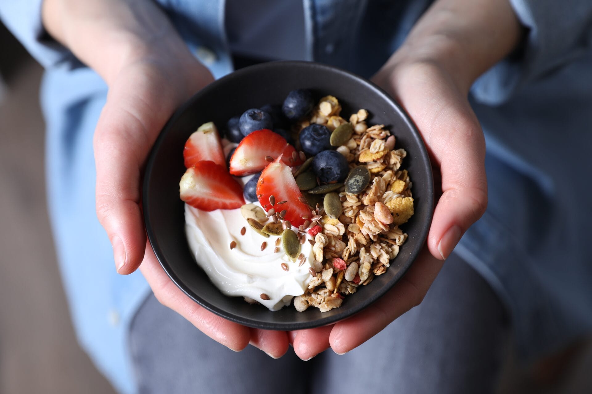 Χέρια κρατούν μπολ με granola, γιαούρτι και φρέσκα μούρα